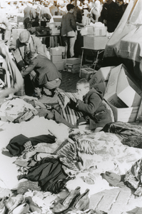 875414 Afbeelding van een jongetje dat op een kussen ligt bij een uitstalling van tweedehands kleding op de rommelmarkt ...